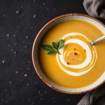 وعاء شوربة باهت اللون مع ملح وأعشاب طازجة وملعقة خشبية جانبية